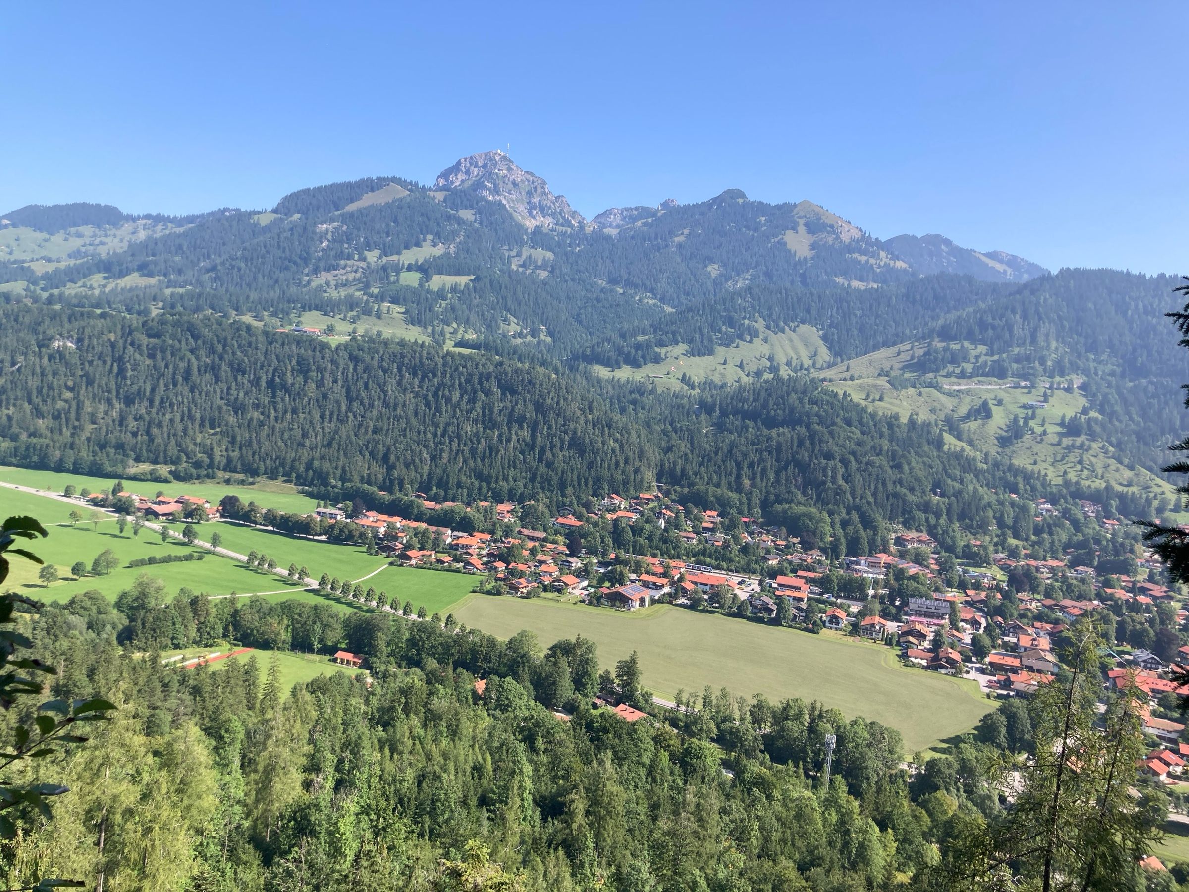 Blick über Wald hinunter auf Bayrischzell im Tal, dahinter der Wendelstein