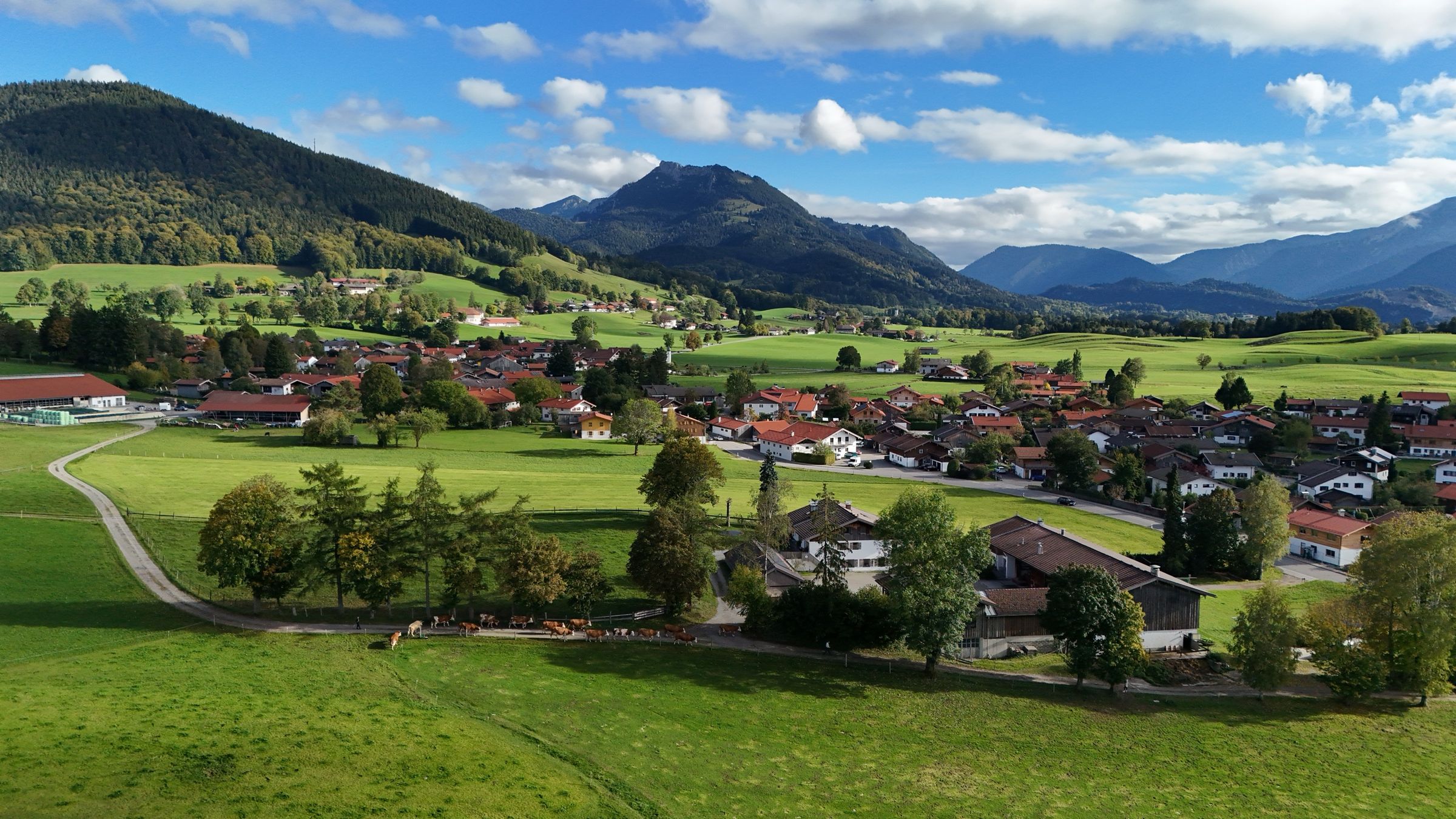 Luftbild über Hundham mit Wiesen und Häusern, dahinter Breitenstein und Wendelstein unter Wolken