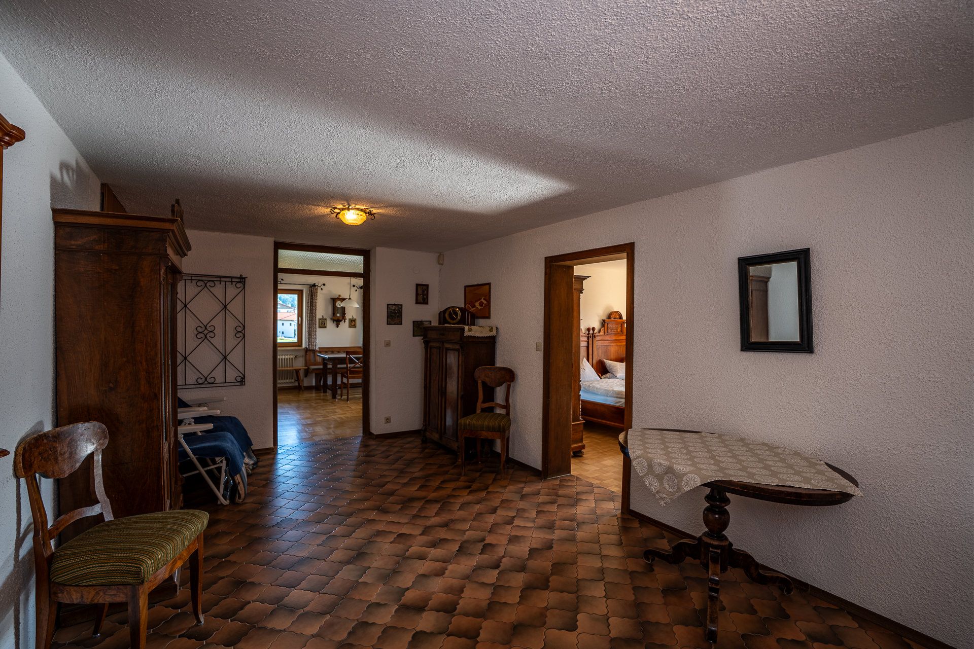 Diele der Ferienwohnung mit Balkon mit Fliesenboden, antikem Schrank, Stuhl und rundem Tischchen, hinten der Blick in die Wohnküche, rechts ins Schlafzimmer mit dem Gründerzeit-Bett
