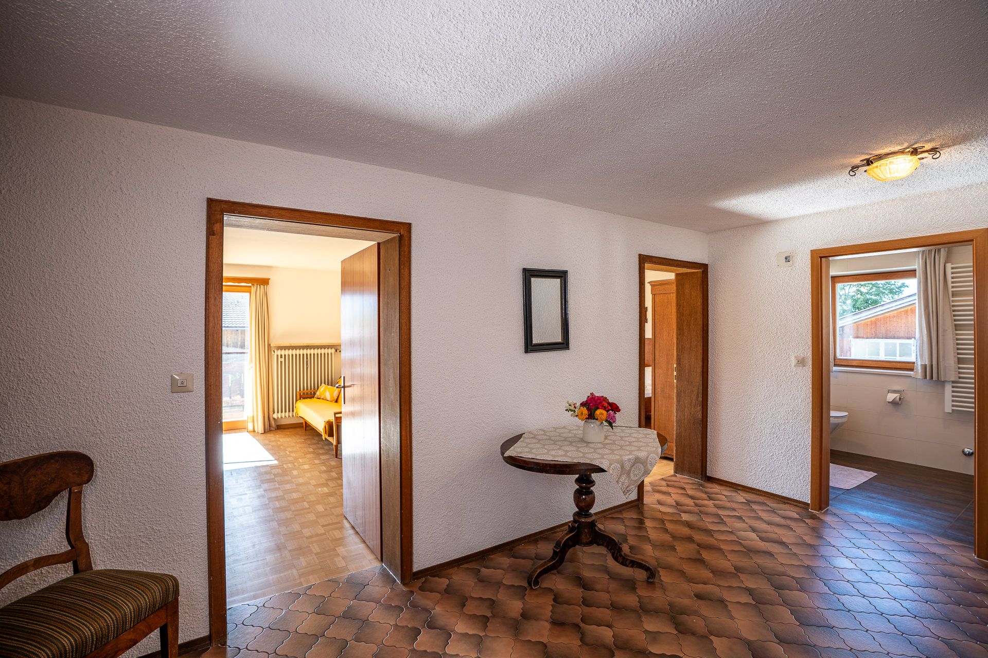 Diele mit rundem Tischchen und Blumen, offene Türen zum Schlafzimmer mit dem gelben Sofa, zu einem zweiten Zimmer und zum Bad
