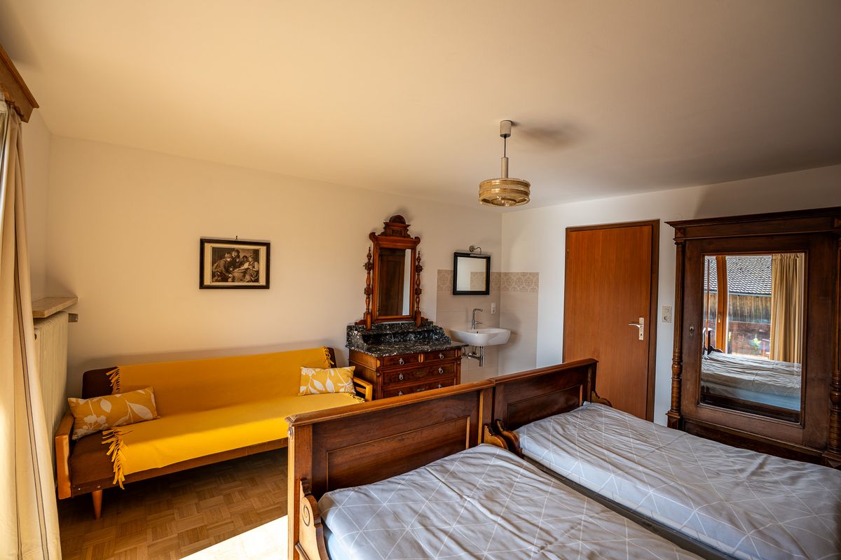 Im selben Schlafzimmer ein gelbes Sofa, ein Waschtisch mit Marmorplatte und Spiegelaufsatz, ein Waschbecken und der Spiegelschrank, vorn das Doppelbett