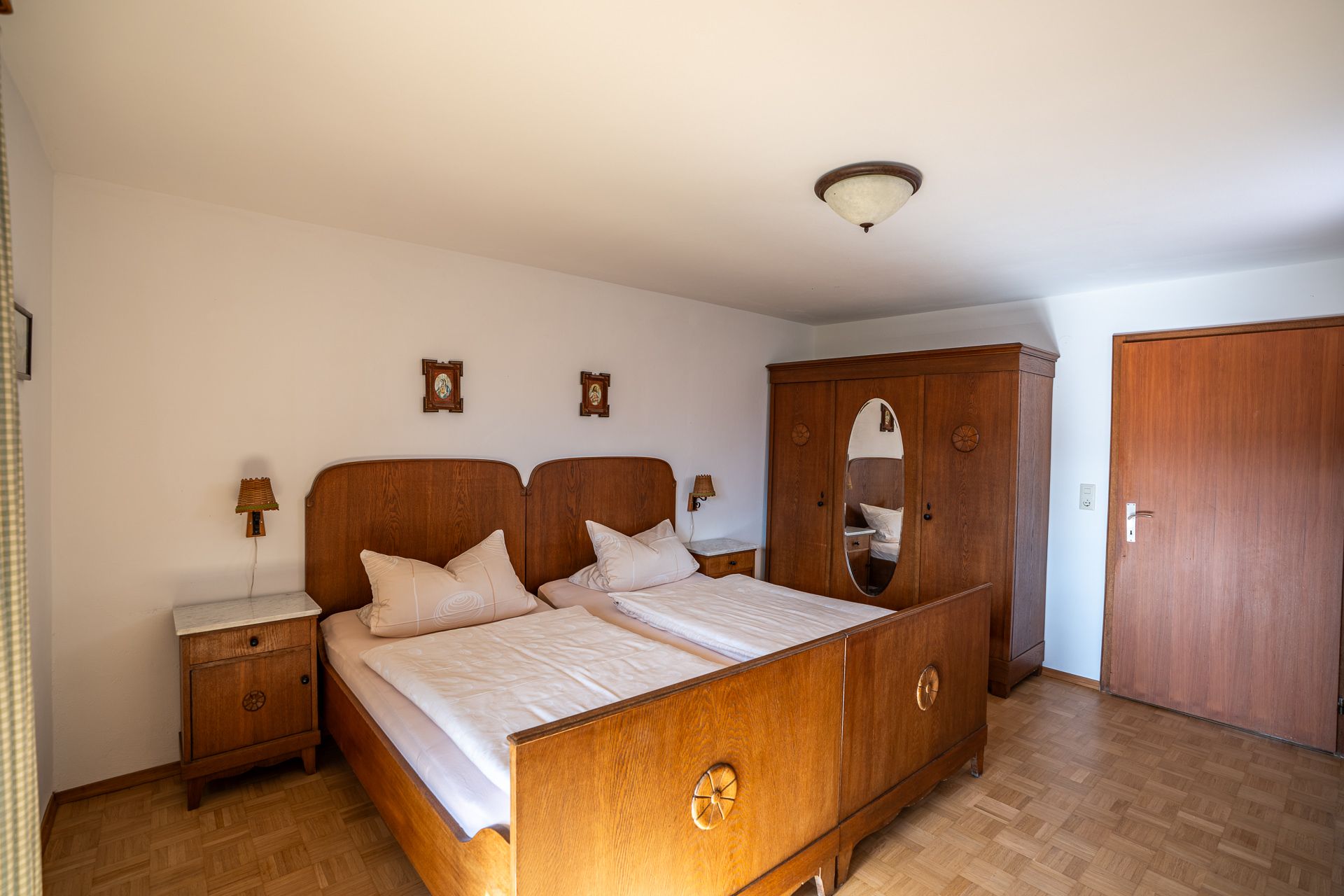 Zweites Schlafzimmer mit Doppelbett aus Holz mit geschnitzten Rosetten, Nachtkästchen mit Marmorplatte und einem Kleiderschrank mit ovalem Spiegel