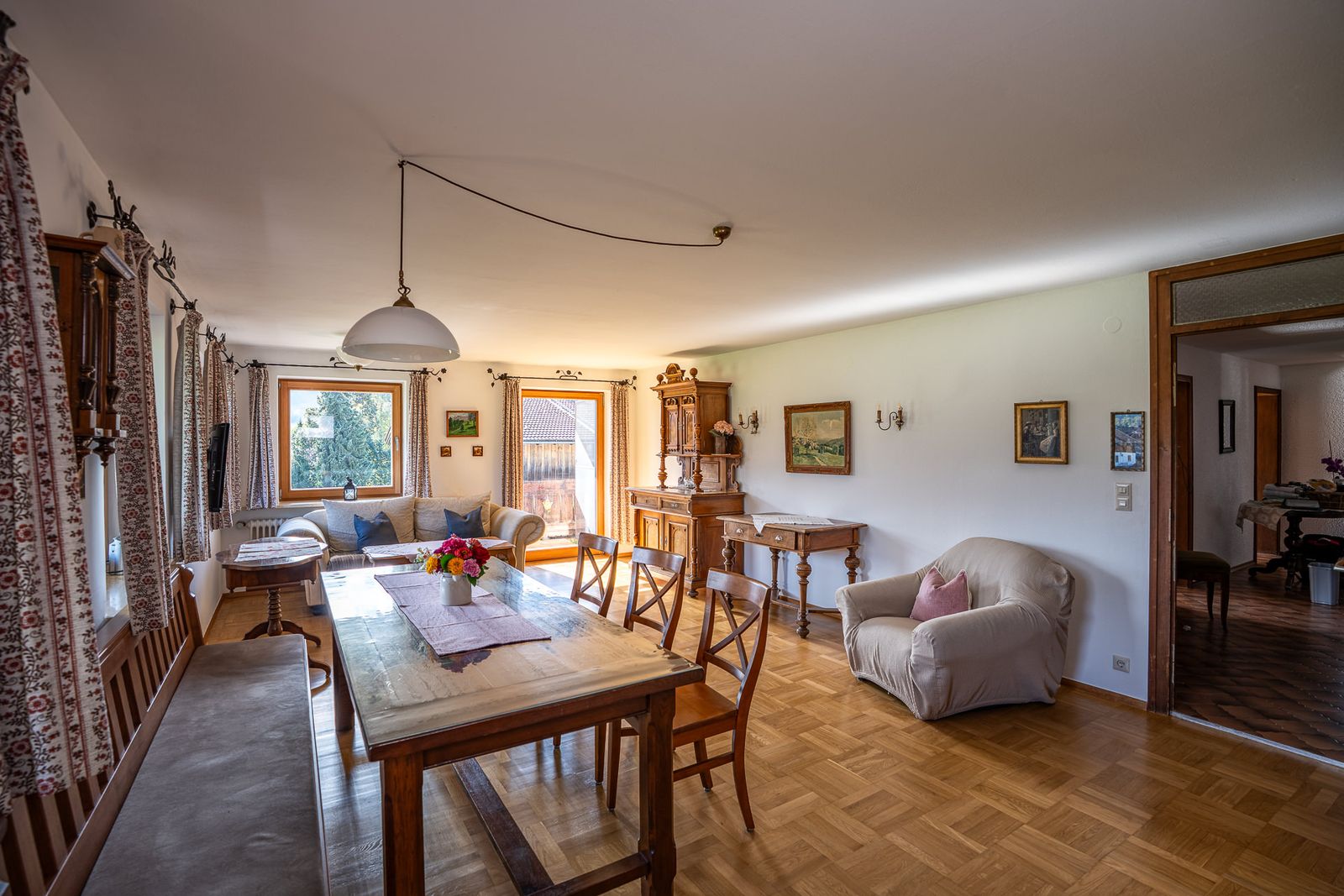 Kitchen-living room of the balcony apartment with a long wooden table, a bench and chairs, with a sofa, an armchair and a carved antique cabinet behind them