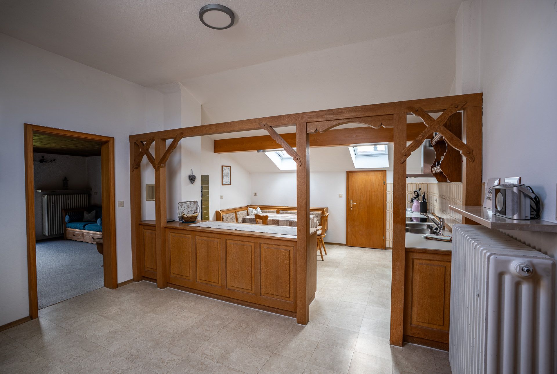 Hallway of the top-floor apartment with wooden arches dividing it from the kitchen, the dining corner below two roof windows behind them and the door to the parlour on the left
