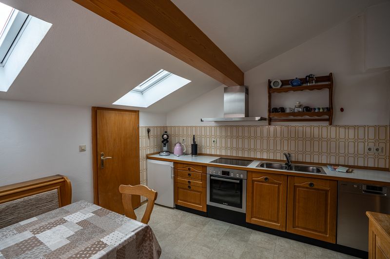 Kitchen units with hob, oven, dishwasher, sink and a small fridge below two roof windows, with an extractor hood and a shelf of cups above