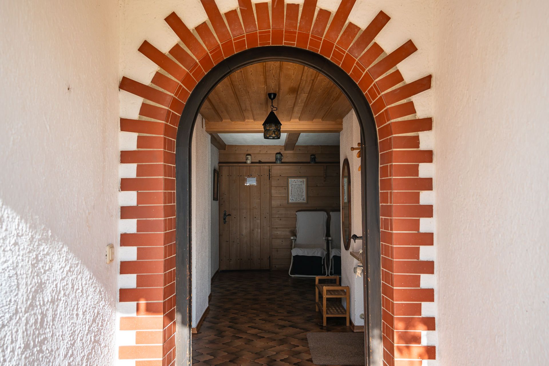 Eingang der Ferienwohnung im Erdgeschoss durch einen Rundbogen aus rotem Backstein, dahinter die Diele mit Holzdecke, Holzwand und einer Laterne