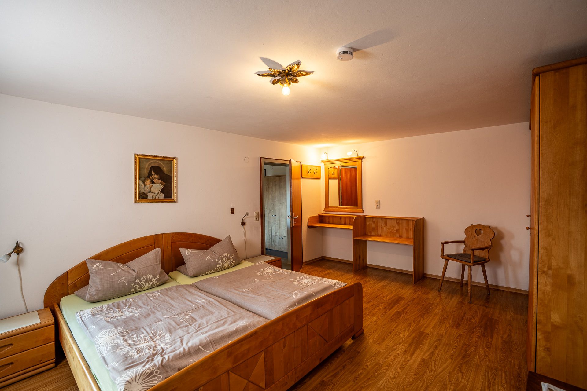 Zweites Schlafzimmer mit Doppelbett, gegenüber ein Frisiertisch mit Spiegel und ein Holzstuhl, rechts ein hoher Kleiderschrank