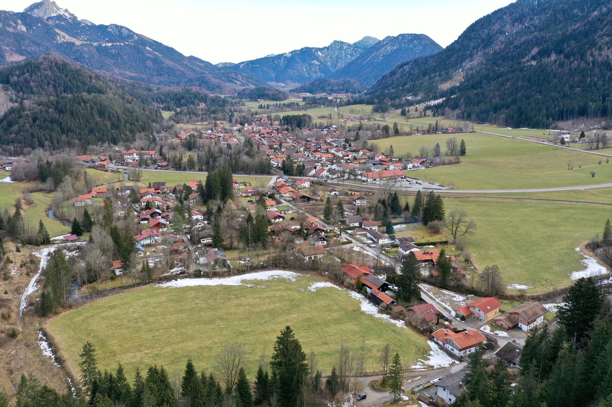 Luftbild des Ortsteils Hammer mit Häusern, Wiesen und Schneeresten, dahinter Berge mit dem Wendelstein