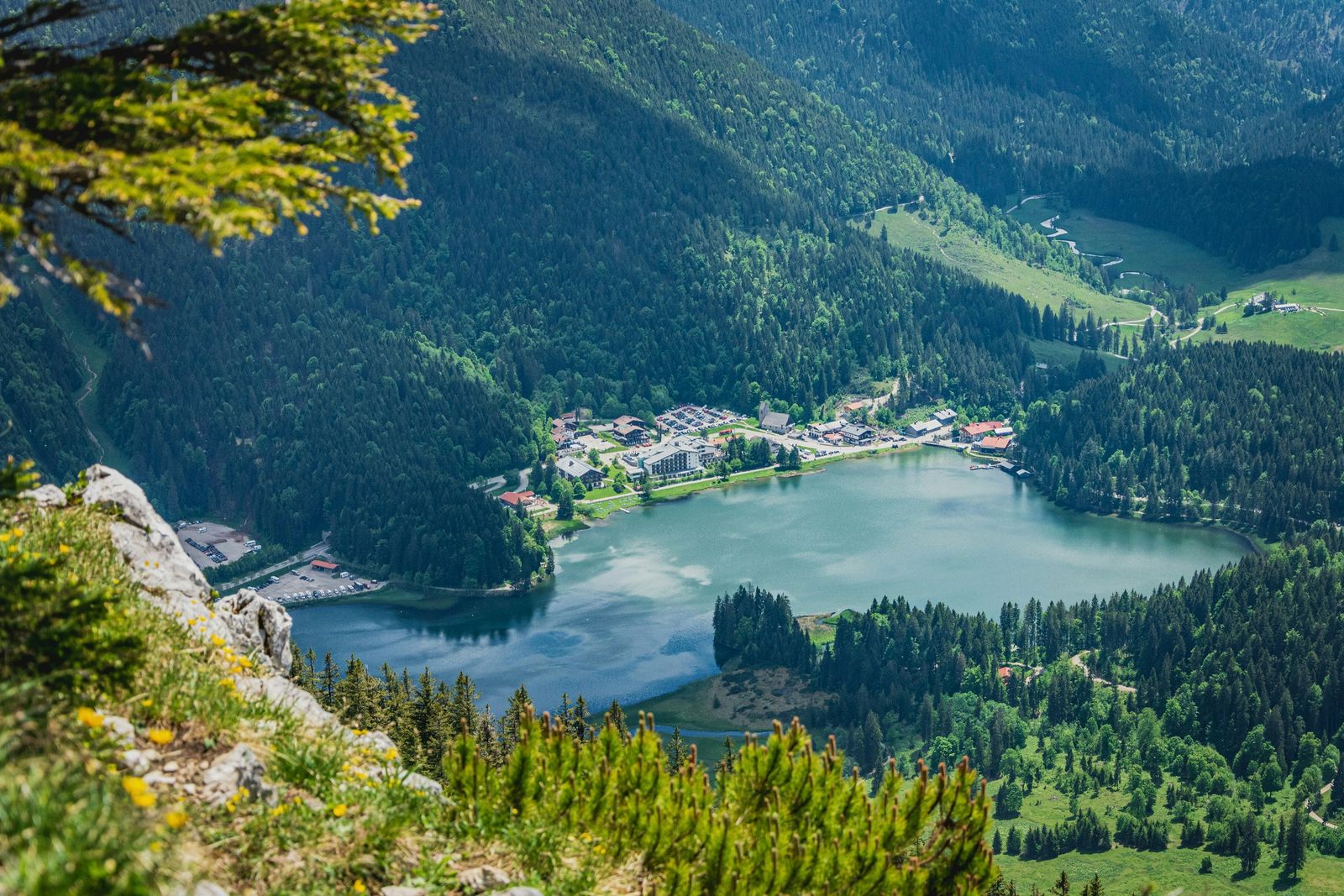 Blick über Fels und Latschen auf den türkisen Spitzingsee mit dem Ort, Hotels und Bergwald