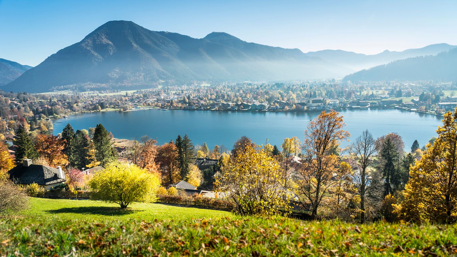 Blick vom Leeberg über buntes Herbstlaub auf die Egerner Bucht des Tegernsees mit Rottach-Egern, dahinter Berge