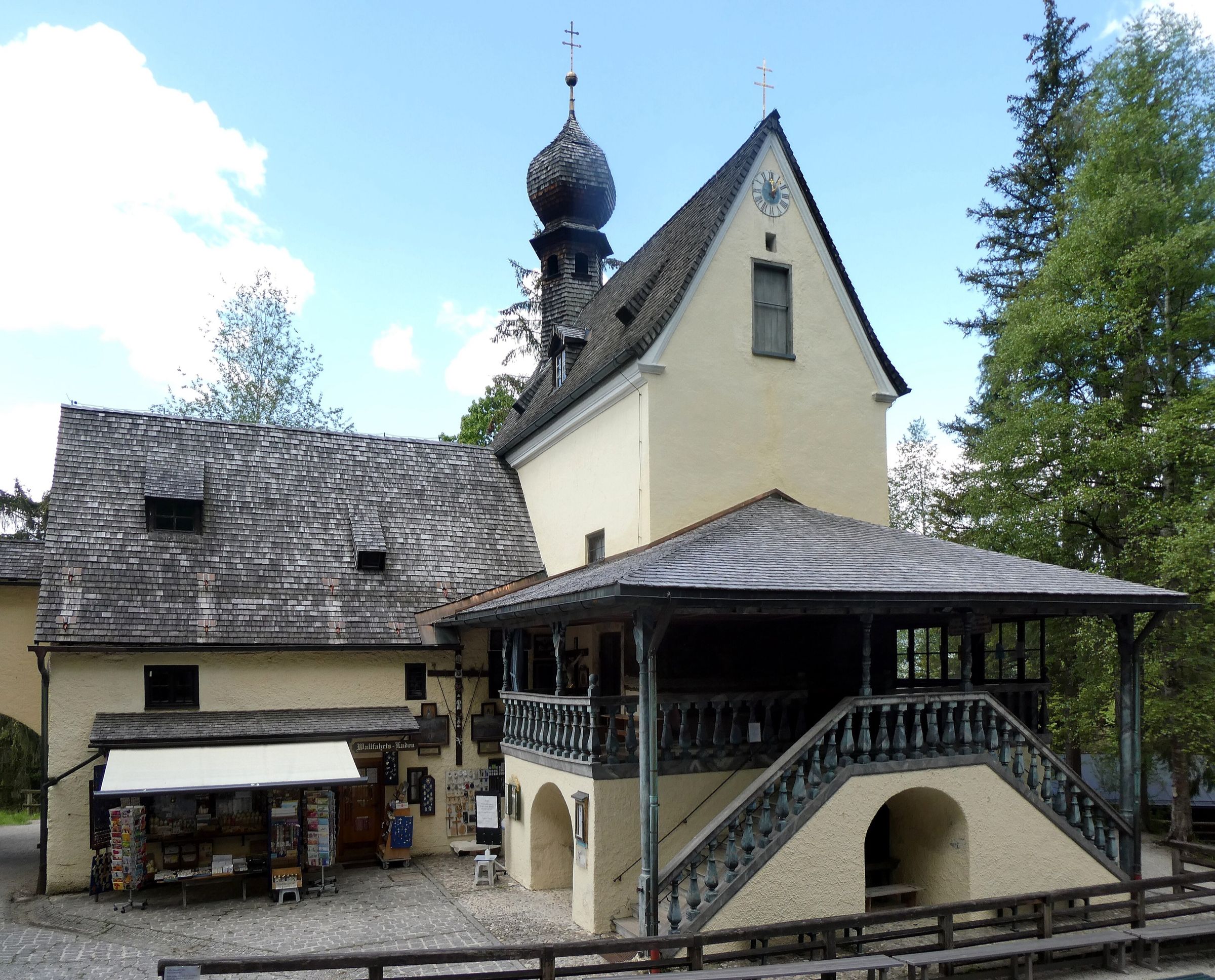 Die Wallfahrtskirche Birkenstein mit kleinem Zwiebelturm und überdachter Freitreppe, daneben Bäume