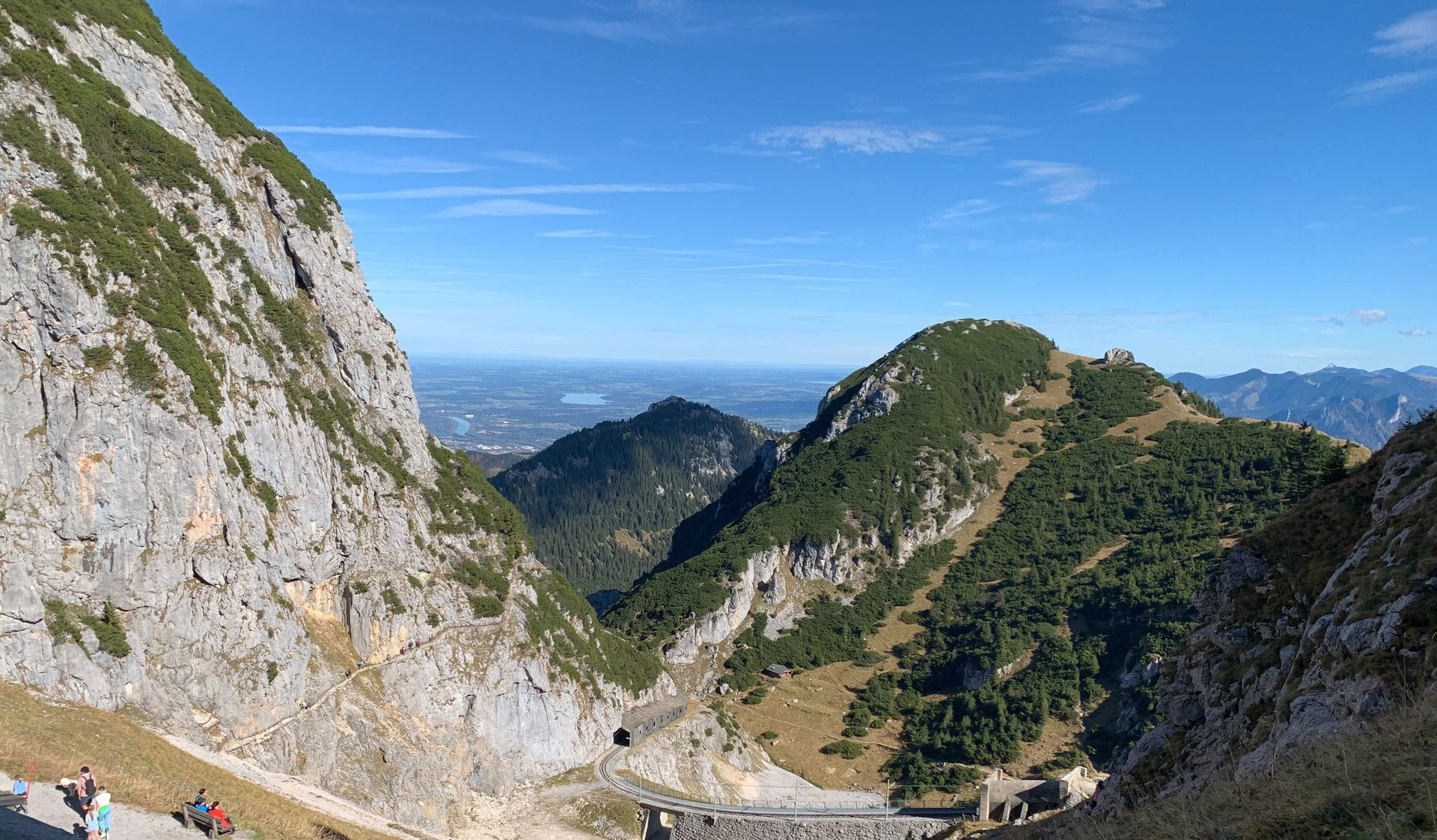 Felswand am Wendelstein, unten ein Weg und die Trasse der Zahnradbahn, dahinter bewaldete Berge und das weite Vorland