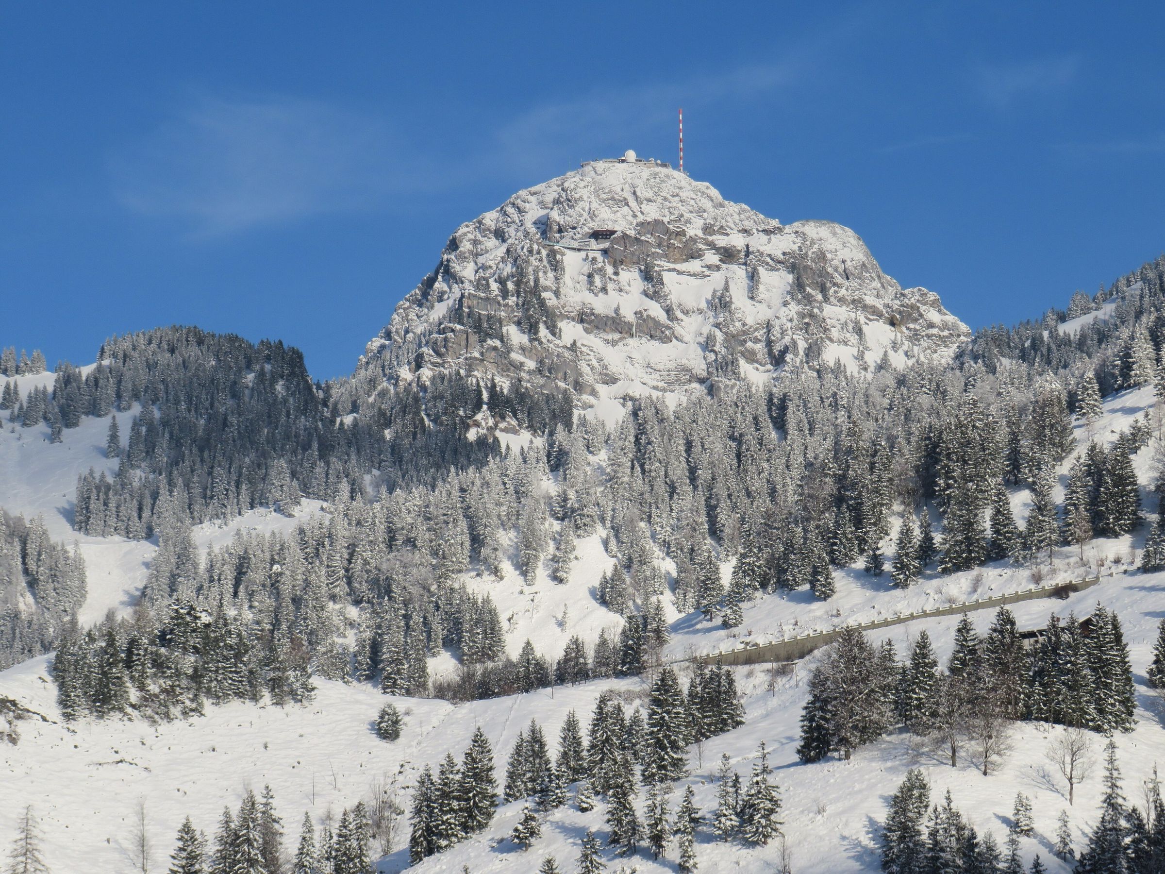 Der verschneite Felsgipfel des Wendelstein mit Sendemast über tief verschneitem Bergwald